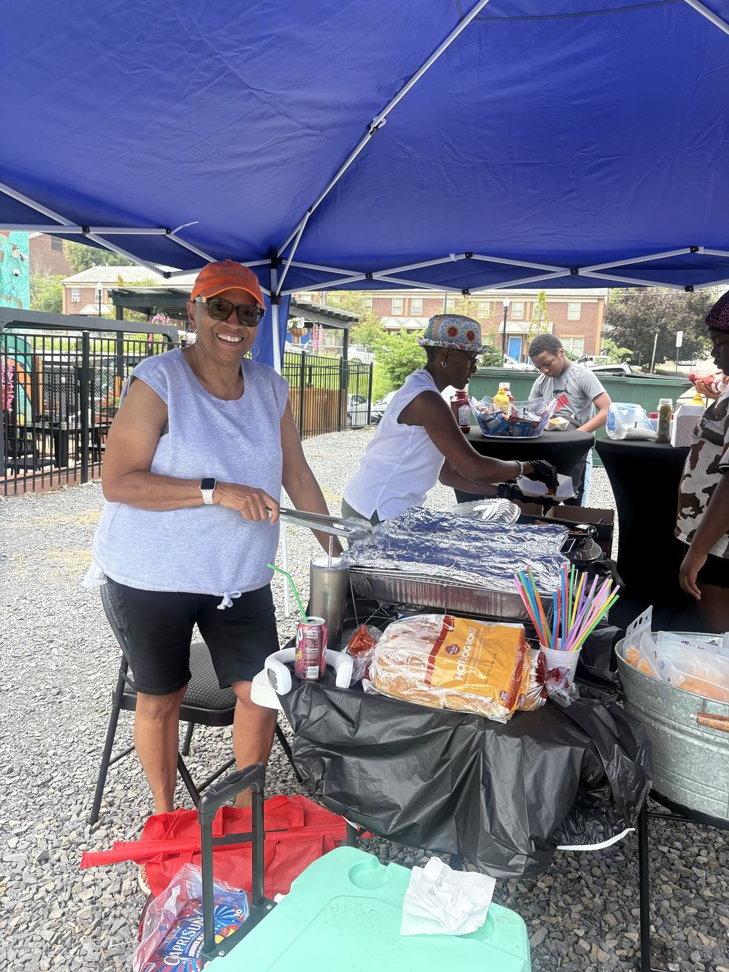 A volunteer smiles while serving food under a tent at a community cookout