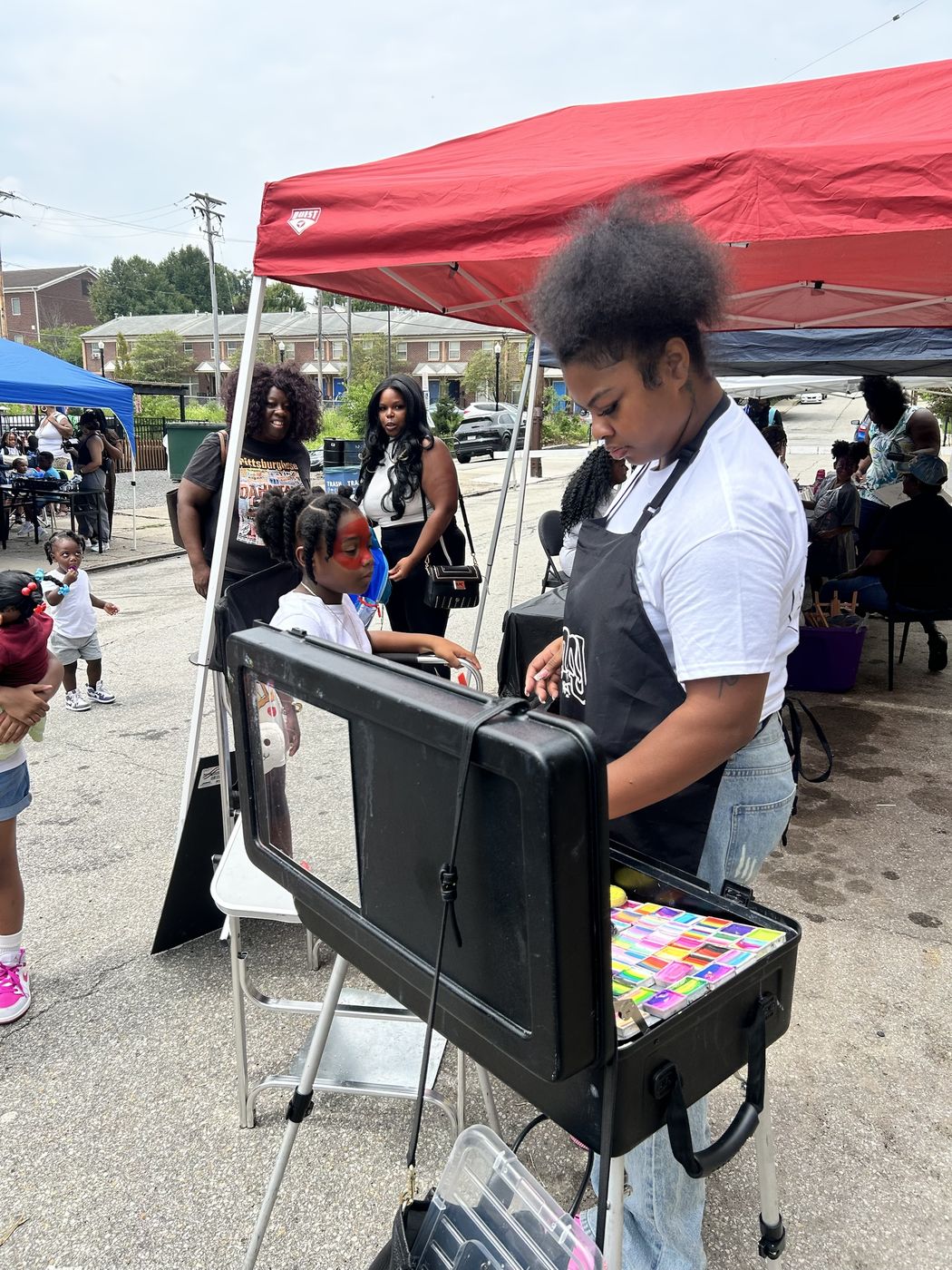 A young artist face paints a child at a community block event