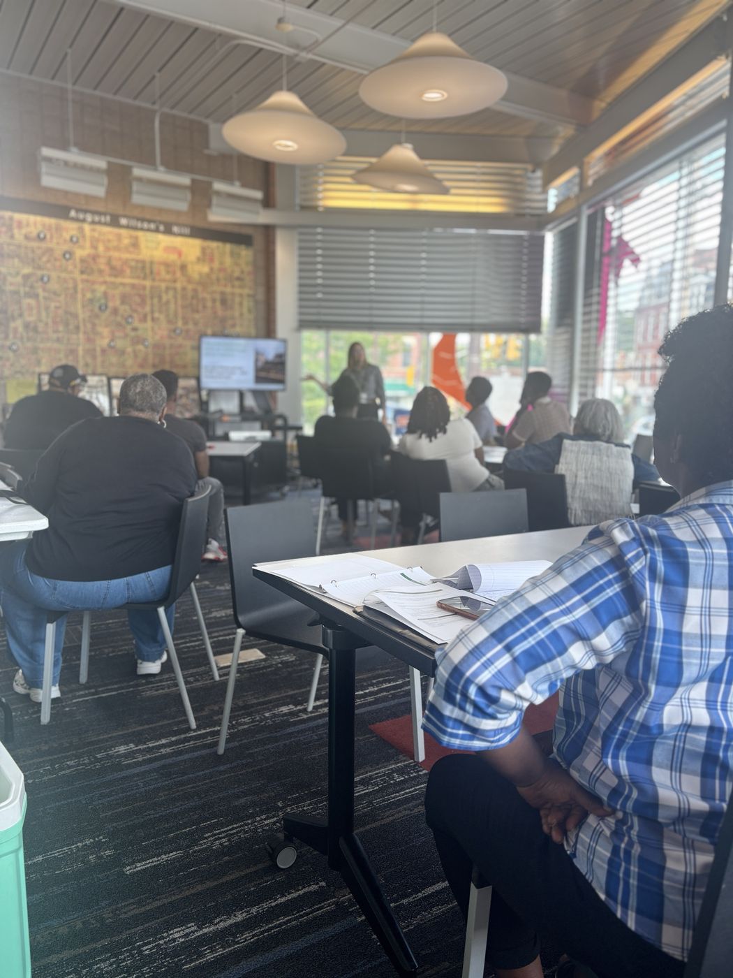 Residents seated at tables listen to a presenter in a community space